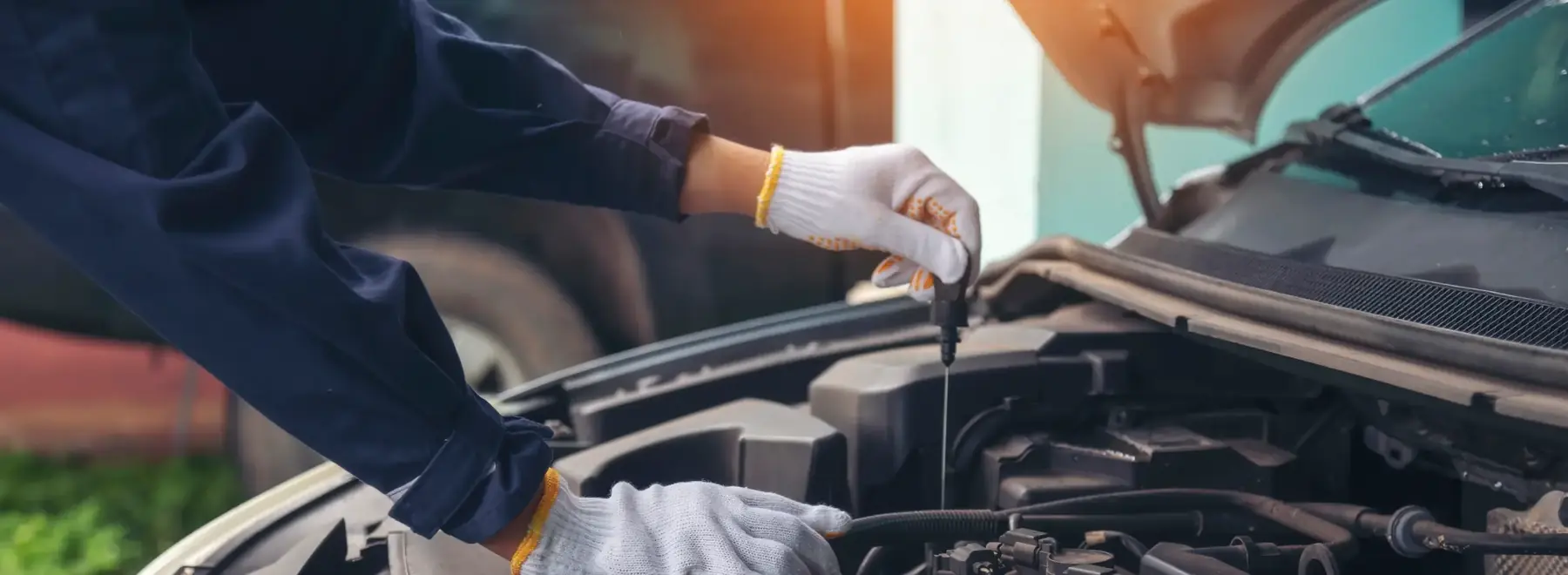 Mechanic in work gloves checking a car&rsquo;s engine oil with the dipstick
